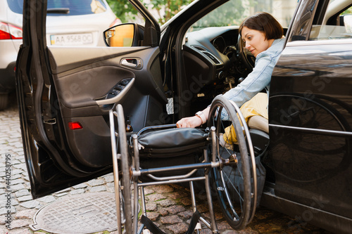 Brunette woman holding wheelchair while getting into car on city street