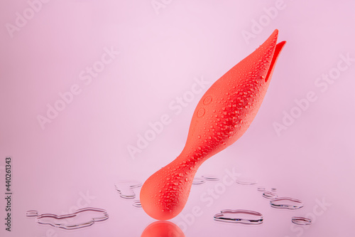 Orange vaginal dildo with vibration on a pink background. Clitoral vibrator located on the mirror. Sex toy covered with drops. Space for text. Image for the sex shop. Toys for adult.