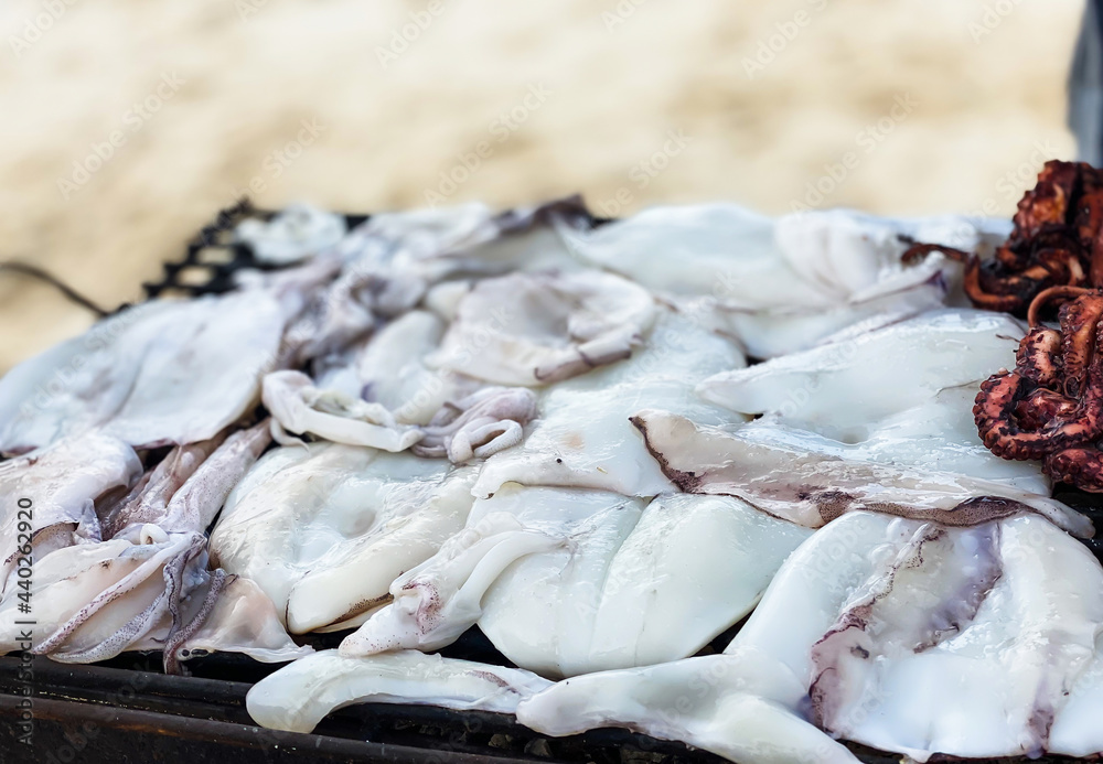 Close-up of squid in the hands of a man fried on a grill on the ocean shore. Close-up of squid in the hands of a man fried on a grill on the ocean shore.