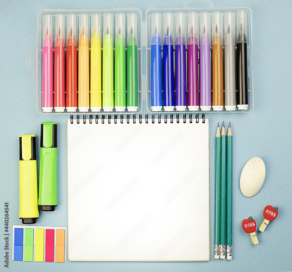 Obraz premium Stationery school supplies on a blue bright background with a notebook in the center, colored markers and pencils. Back to school. School learning concept. Copy space.