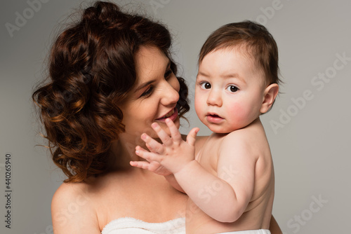 smiling mother holding son in arms isolated on grey