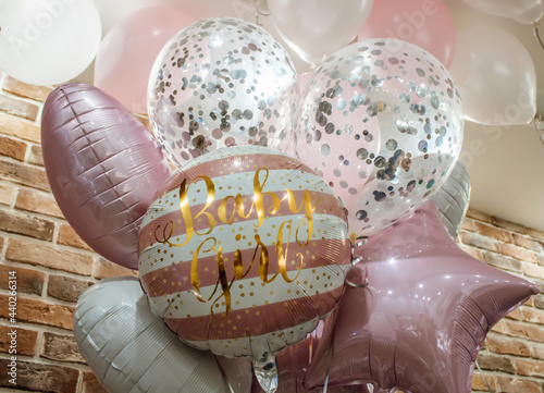 Several shiny balloons in a pink color scheme, filled with helium, joined together in a beautiful bouquet on a brick wall background. Decoration of the holiday dedicated to the birth of a girl. Congra photo