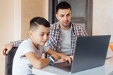 Young father and kid son using laptop at home for child education, looking at screen doing online learning