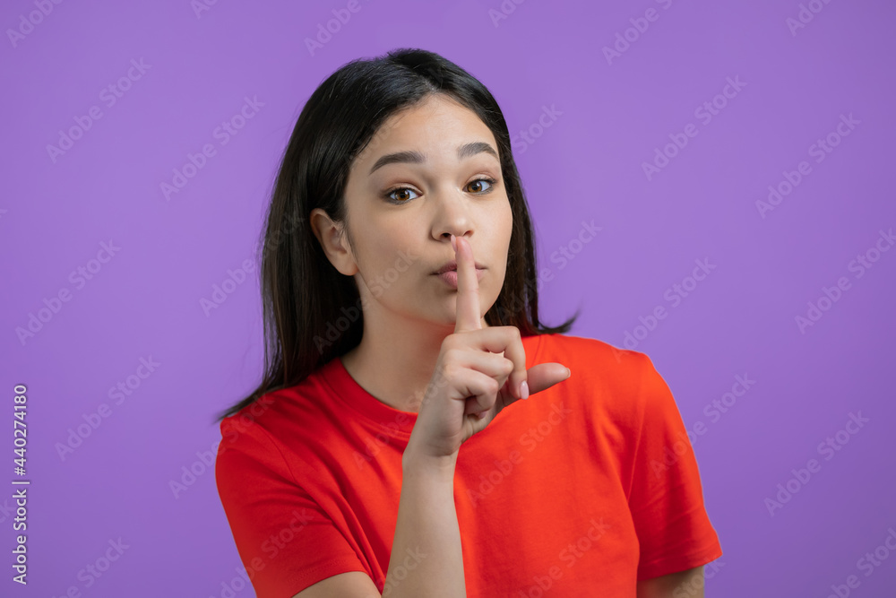Smiling woman holding finger on her lips over violet background. Gesture of shhh, secret, silence. Close up. Smiling woman holding finger on her lips over violet background. Gesture of shhh, secret, silence. Close up.