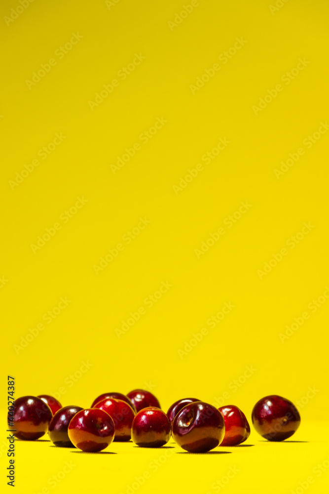 A bunch of ripe red cherries lies chaotically on a bright yellow summer background with plenty of space for insertion. A bunch of ripe red cherries lies chaotically on a bright yellow summer background with plenty of space for insertion.