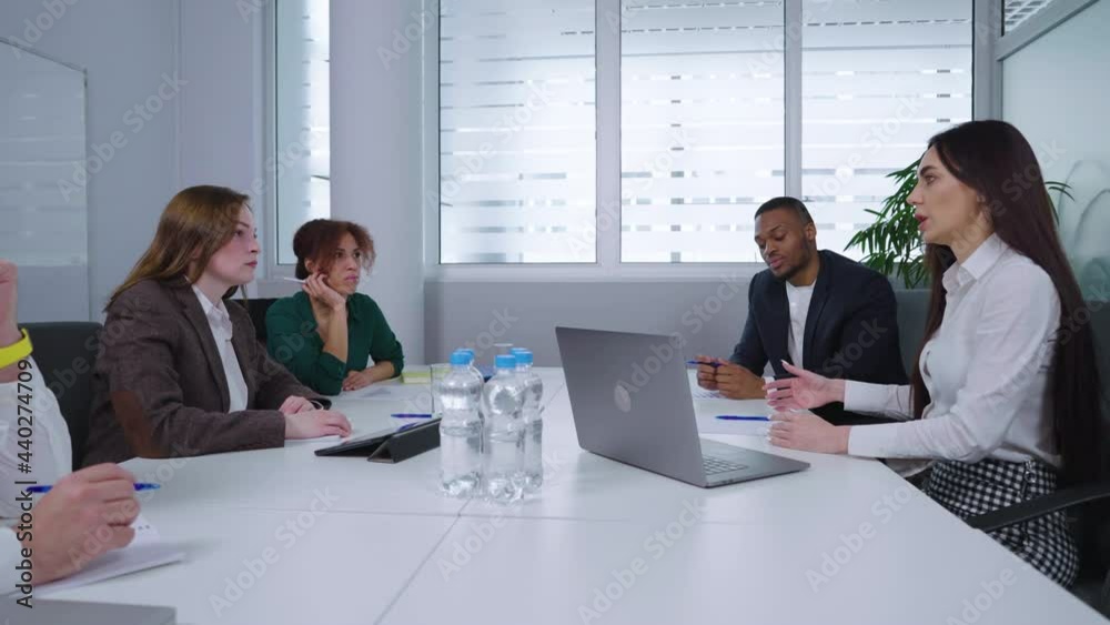 Diverse executives sitting at table with laptops, tablet and bottled water and having discussion. Arc shot serious men and women planning company strategy. Concept of business meeting Diverse executives sitting at table with laptops, tablet and bottled water and having discussion. Arc shot serious men and women planning company strategy. Concept of business meeting
