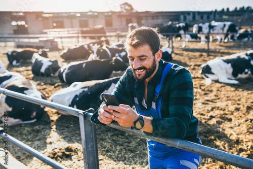 Wallpaper Mural Happy young farmer standing in fornt of cows and looking at his phone. Torontodigital.ca