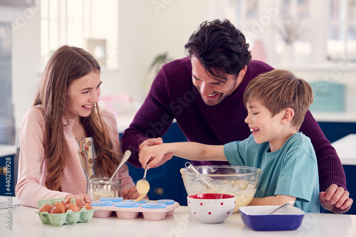 Father With Two Children In Kitchen At Home Having Fun Baking Cakes Together