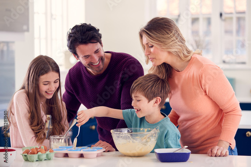 Family With Two Children In Kitchen At Home Having Fun Baking Cakes Together