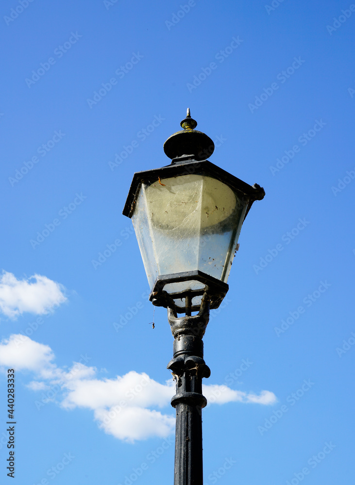 Old black metal street lamp. Blue sky with clouds in the background. Old black metal street lamp. Blue sky with clouds in the background.