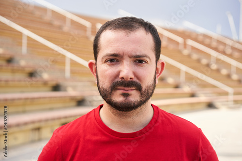 Outdoor portrait of an ugly man looking at the camera with serious face. Close-up of a serious male face. Concept of people and emotions. Red t-shirt.