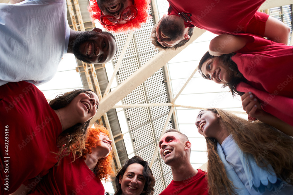 Obraz premium View from below of a group of people celebrating together and hugging while cheering for their sports team from a stadium. Cheerful fans watch the game in costume at the stadium.