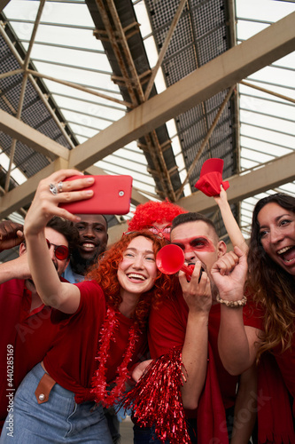 Vertical photo of a group of people taking a smiling selfie while cheering for their sports team from a stadium. Cheerful fans take a cell phone photo while celebrating at the stadium. photo