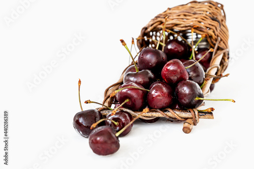 Overturned wicker basket with ripe sweet cherries spilling out of it on white background © Gioia