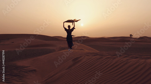 Portrait of a young Arab woman wearing traditional black clothing during beautiful sunset over the desert.