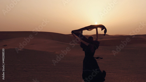 Portrait of a young Arab woman wearing traditional black clothing during beautiful sunset over the desert. photo