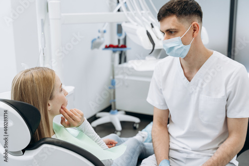 Dentist in a protective mask communicates with an attractive patient. The dentist works in the dental office