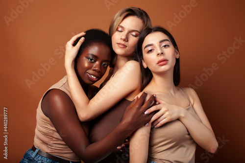 young pretty caucasian, afro, asian, scandinavian woman posing cheerful together on brown background, lifestyle diverse nationality people concept