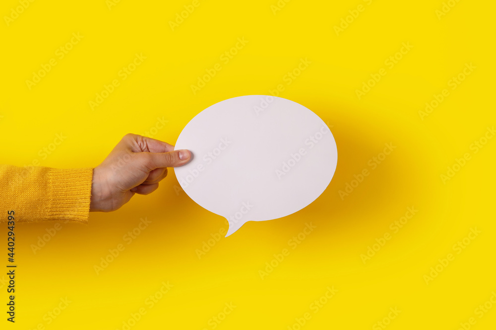 Hand holding a white round blank speech bubble over yellow background Hand holding a white round blank speech bubble over yellow background
