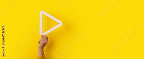 3d media play button in hand over yellow background, panoramic layout