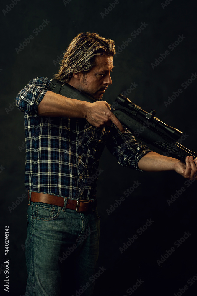 Fototapeta premium Man with blond hair in lumberjack shirt and jeans aims a shotgun.