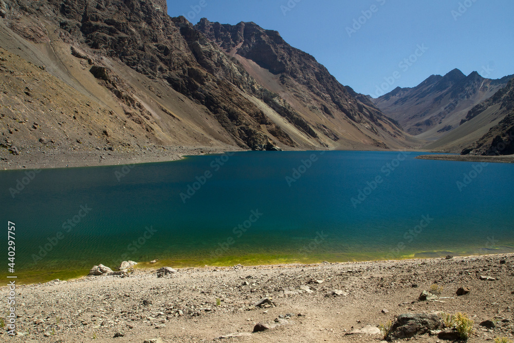 The deep blue color water lake very high in the Andes mountains. View of the Inca Lagoon in Chile, surrounded by rocky mountains and cliffs.