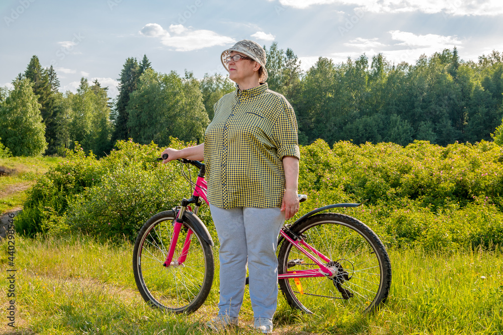 Obraz premium Elderly woman with a bike on the path. Grandma rides a bike.