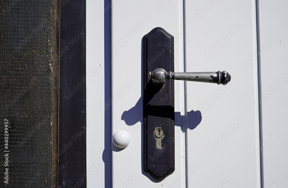 Old black metal door handle on a white wooden door. Close-up of locked door with keyhole. Old black metal door handle on a white wooden door. Close-up of locked door with keyhole.