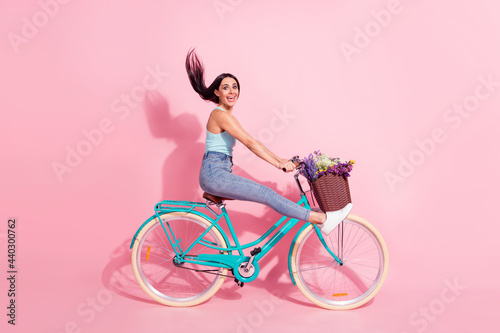 Full length body size photo of smiling woman riding bicycle isolated on pastel pink color background © deagreez