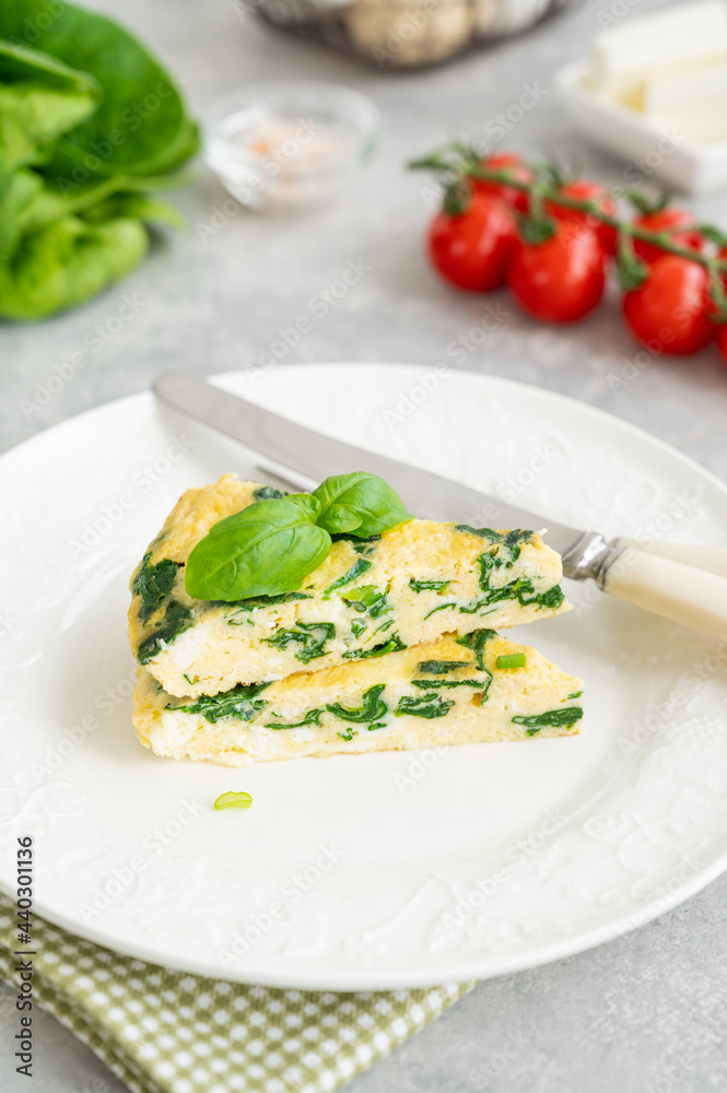 Omelette with spinach, green onions and feta cheese on a white plate on a gray concrete background. Healthy breakfast. Copy space.