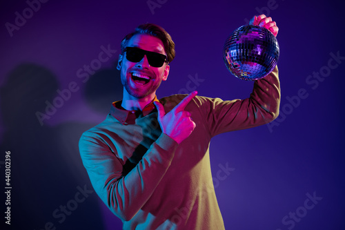 Photo portrait of man smiling in sunglass pointing finger disco ball music isolated purple color background © deagreez