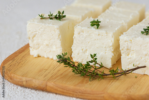 Paneer, tofu,  soy cheese,  or brynza, feta with thyme  on a wooden cutting board on a light background