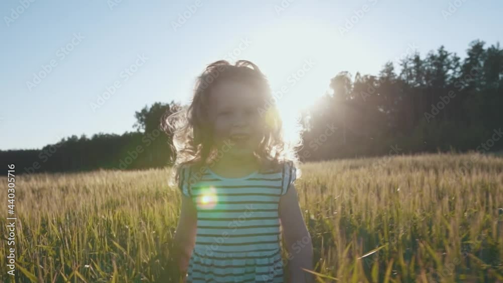 Happy little girl walks in slow motion across field in warm sunshine in a wheat field on sunset background. Cute joyful child touches the ears and laughs with happiness. High quality FullHD footage Happy little girl walks in slow motion across field in warm sunshine in a wheat field on sunset background. Cute joyful child touches the ears and laughs with happiness. High quality FullHD footage