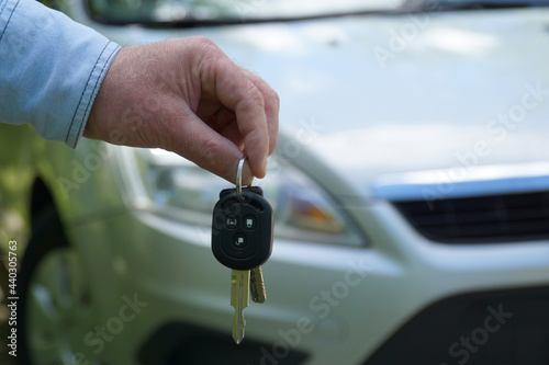 The man holds the keys against the background of the car. The concept of buying or renting a car and summer travel. Car theft prevention concept.