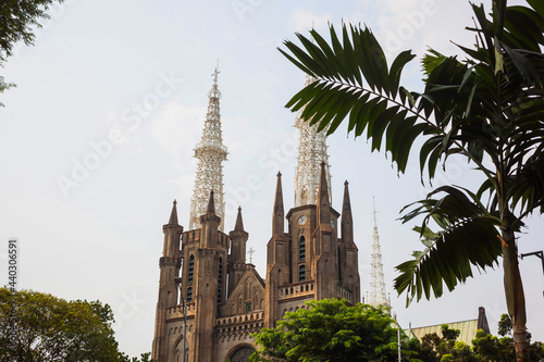 A beautiful cathedral for Indonesian christian believers in Jakarta, Indonesia. Divine temple in gothic style behind a tropical palm tree on a summer day.