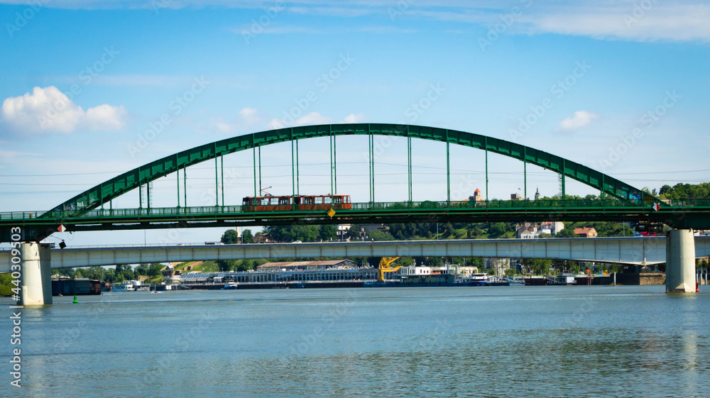 Naklejka premium The old green railway bridge with a passing red tram over the Sava river in Belgrade