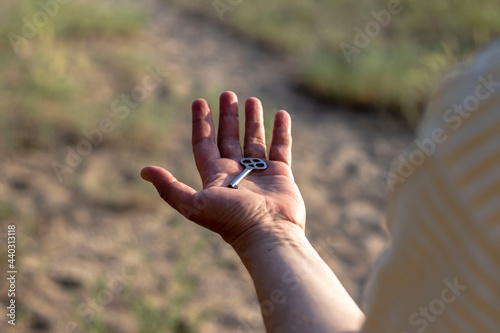 A Caucasian man holds a metal key in his palm on his outstretched hand in front of him. Close-up with blurred background back view.