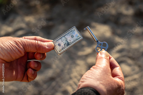 A Caucasian man is holding a metal key and a metal keychain in the form of a paper dollar. Top view close-up with blurred background.