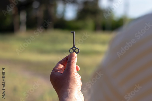A Caucasian man holds a metal key in his palm on his outstretched hand in front of him. Close-up with blurred background back view.
