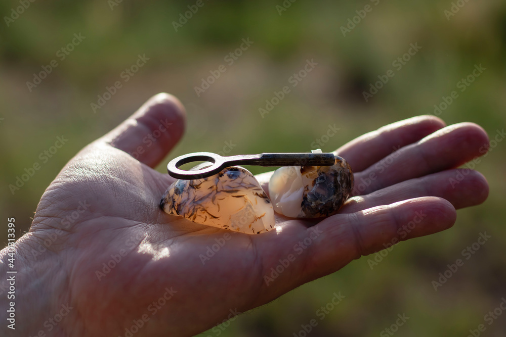 In the palm of a man there is a semiprecious agate stone and a metal key in bright sunlight. Close-up with blurred background.