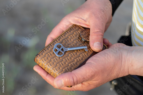 A Caucasian man holds a brown leather wallet with a metal key to the apartment. Close-up with blurred background.