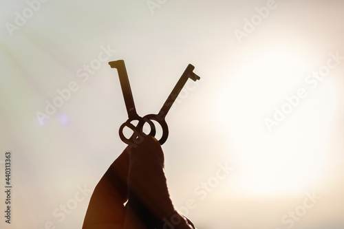 Two metal keys in a man's hand raised up against the background of the sky in bright sunlight. Close-up with blurred background.