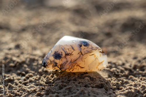 A semi-precious stone agate lies on the sand in bright sunlight. Close-up with blurred background.