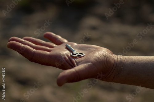Old shiny metal key on a man's palm in bright sunlight. Close-up with blurred background.