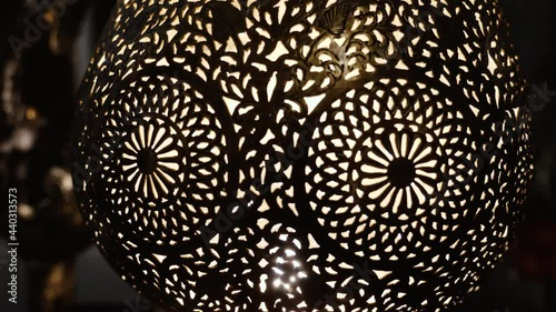 A lit, Moroccan, Arabic brass lamp with intricate floral pattern. Concept for Moroccan and Arabian lamp design. Zooming in through the pattern into the inside of the lamp.