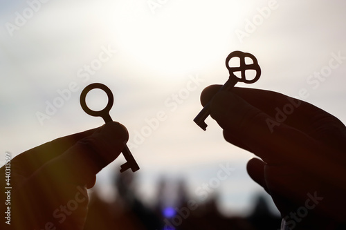 A Caucasian man holds in his hands two different metal keys to the lock in the backlight. Close-up with blurred background.