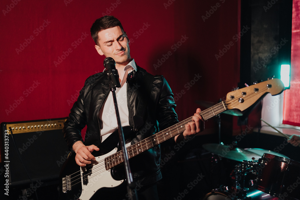 Obraz premium Talented handsome young guitarist man singing a song in studio recording on red background surrounded by instruments. Passion, hobby, singer, electric guitar