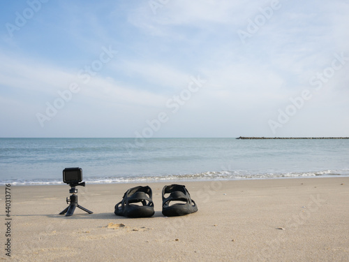 sport camera lay on the white sand beach beside the sandle with space of blue sky