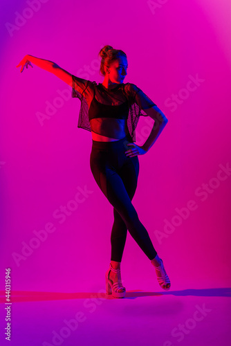 Beautiful female dancer wearing black and high heels while performing pole dance tricks