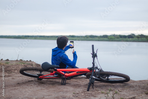 Young cyclist taking a selfie, resting on the ground next to his bike, active lifestyle.